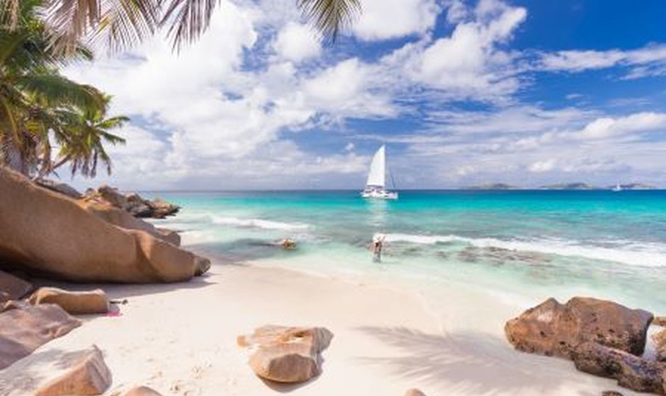 Sandy Seychelles Beach with people, sailing boat, blue sky